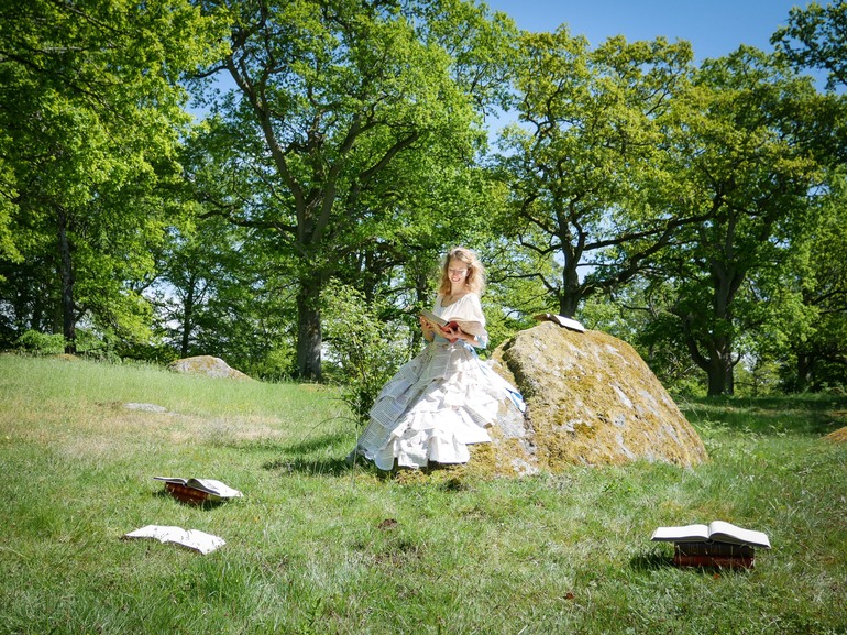 Deltagare sitter på en sten och läser en bok iförd klänning gjord av boksidor
